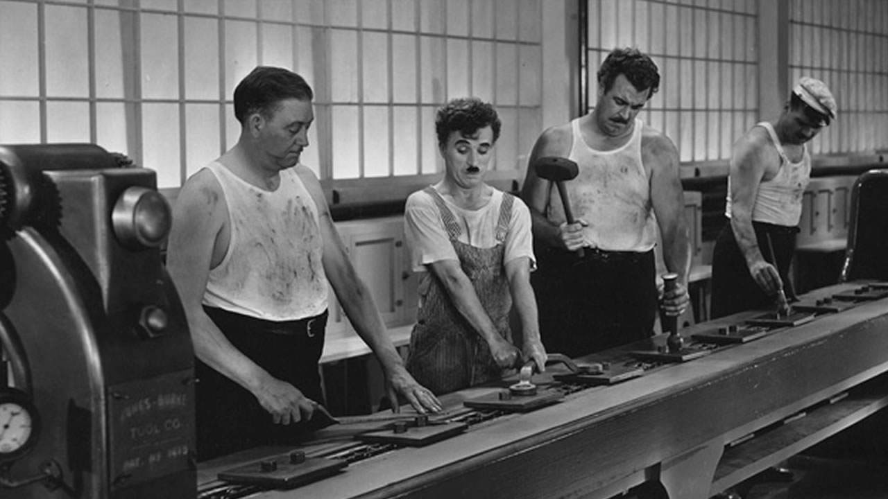 Chaplin e outros trabalhadores matelando peças sem propósito claro a eles. Alienação do trabalho.